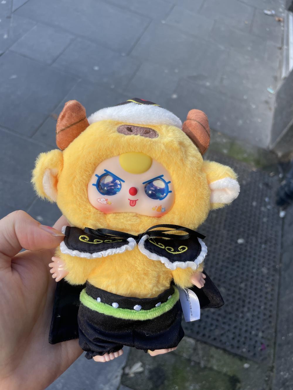 gab holding a yellow creature with horns and big blue eyes and a black cape