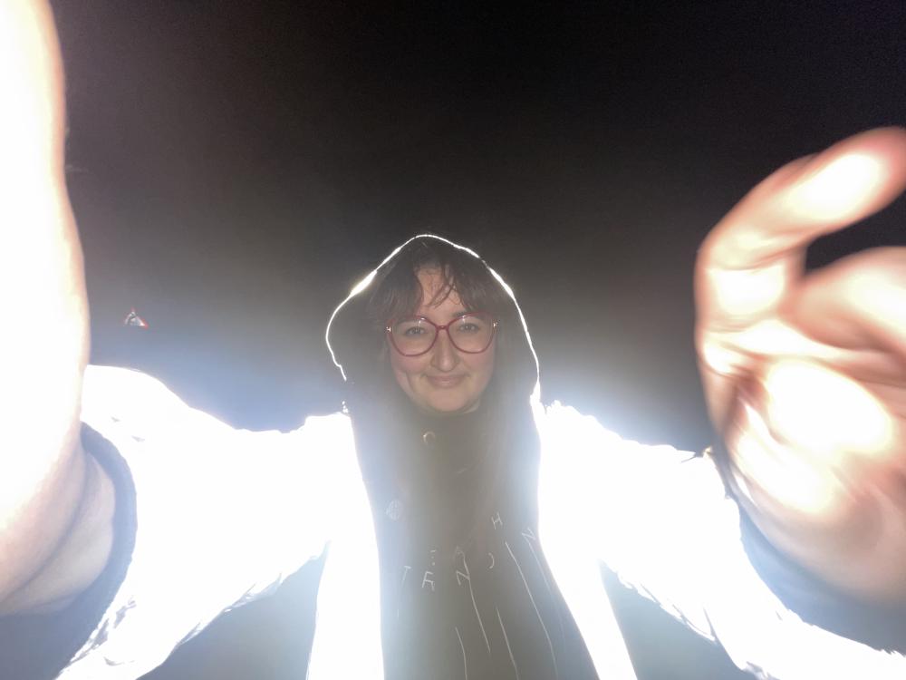 gab takes a selfie wearing a reflective silver jacket and smiling in darkness