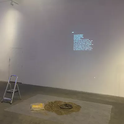 a paragraph of tiny text is projection on a wall, and in front of it there is a step ladder, and a pile of sand