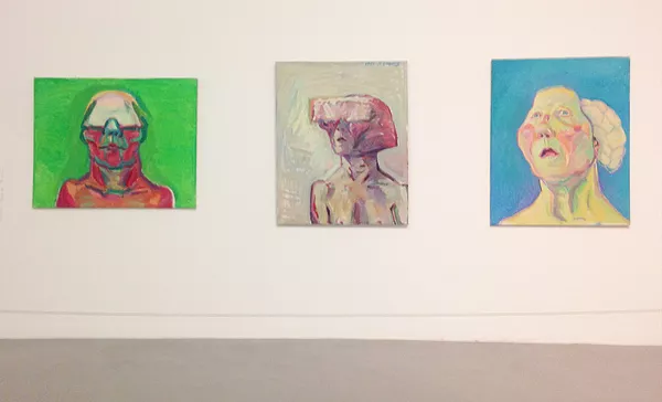 three paintings by Maria Lassnig, three heads, two wearing what look like VR goggles or whatever is closer to that time period, and another that looks like its brain is falling out