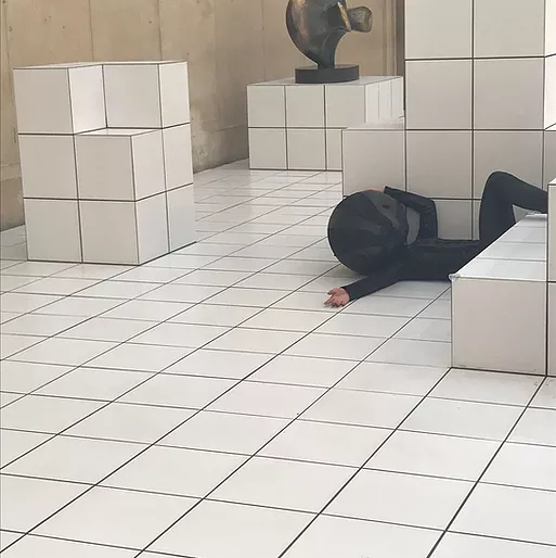 one of the performers in all black lies back with a hand on their head over the while tiles in a dramatic but comfortable pose