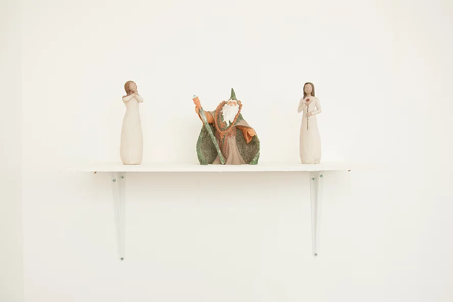 a shelf has two wooden women on it and in between them there is a wizard with a green cloak on