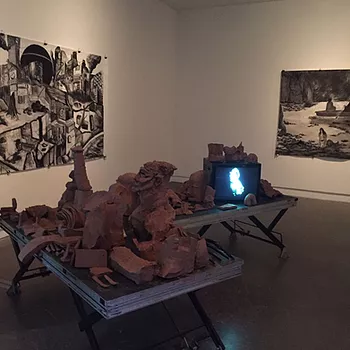 there&rsquo;s a CRT on a table with more brown pieces of clay ceramics piled around it on a table at the centre of a gallery, all indeterminate objects