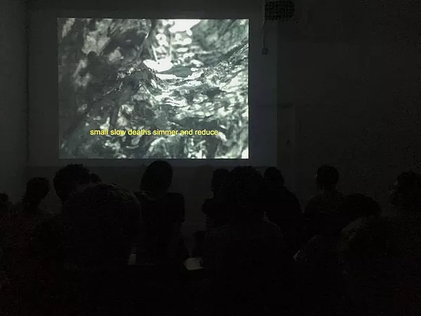 an abstract digital image of different shapes and marks are stretched across a projection in a room full of people