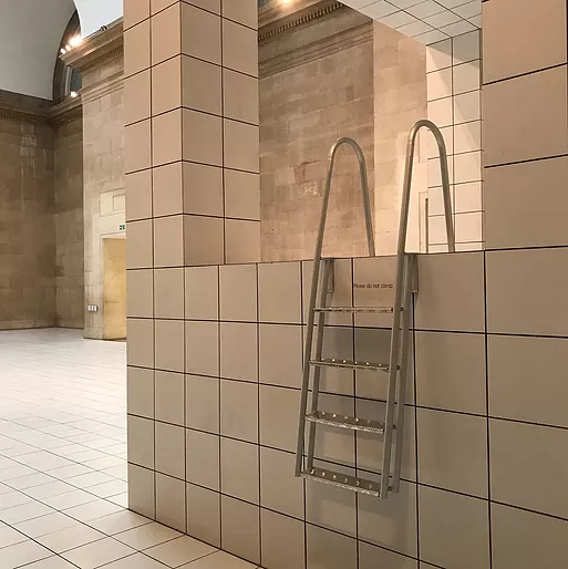 at the edge of one of the tiled walls that is rising up out of the tiled floor, there is a step ladder with big handles at the top like you&rsquo;d see at the entrance of a swimming pool