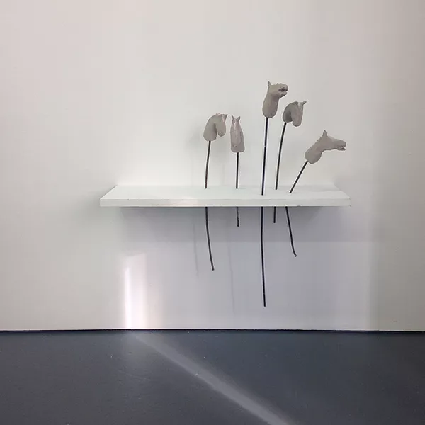 a white shelf on the wall has metal rods pierced through it and off the rods are clay horse heads