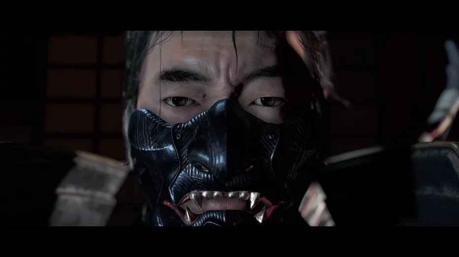 A close up of Jin&rsquo;s face as we wears a mask over the lower part of his face that looks like a black demon with fangs