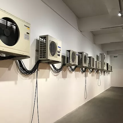 outdoor air conditioners are running all along the wall, and connected to one another with drooping black wires