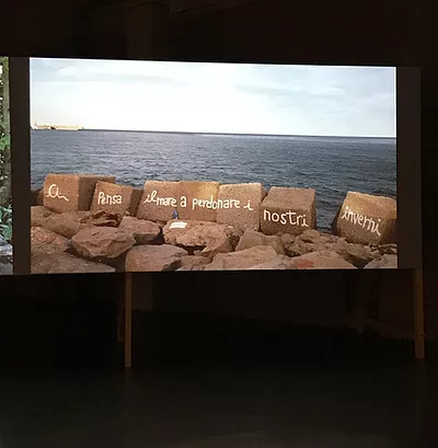 a shot of rocks with italian graffiti on them at the edge of the sea