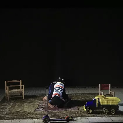 the same shot of the kid hanging onto the man praying except now they are doing it on a stage in a black room with the same carpet and toys around him setting the scene