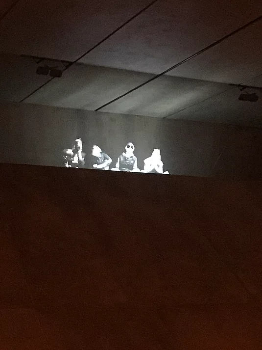 at the top of the sloping concrete, there is a black and white projection of four kids sitting there