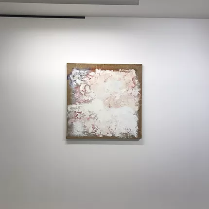 a canvas is almost completely covered in white paint that is blurred out, and it looks in parts like it is covering other colours below, and the edges are still visible of a hessian canvas