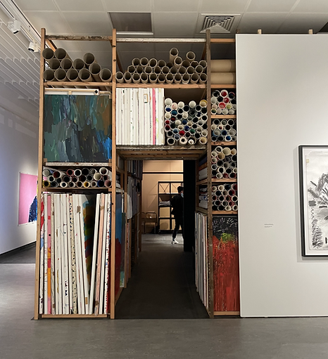 a sectioning wall in the gallery looks like an artist studio&rsquo;s storage, with shelves full of canvases and rolls of paper and cardboard