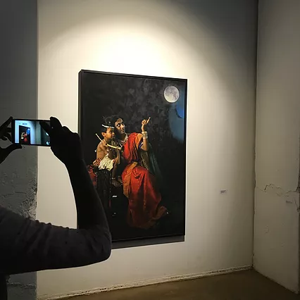 a brown woman and her child sit looking and pointing up at the moon in a staged portrait