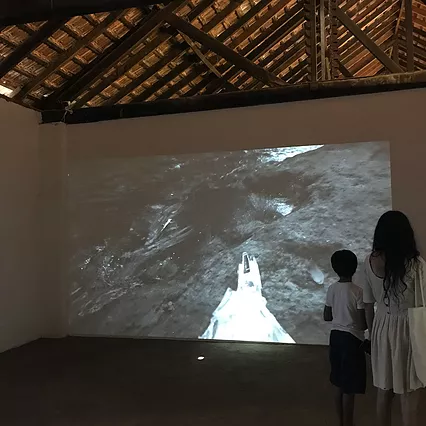 a woman and a child stand looking at a projection in black and white of a white triangular shape against rocks