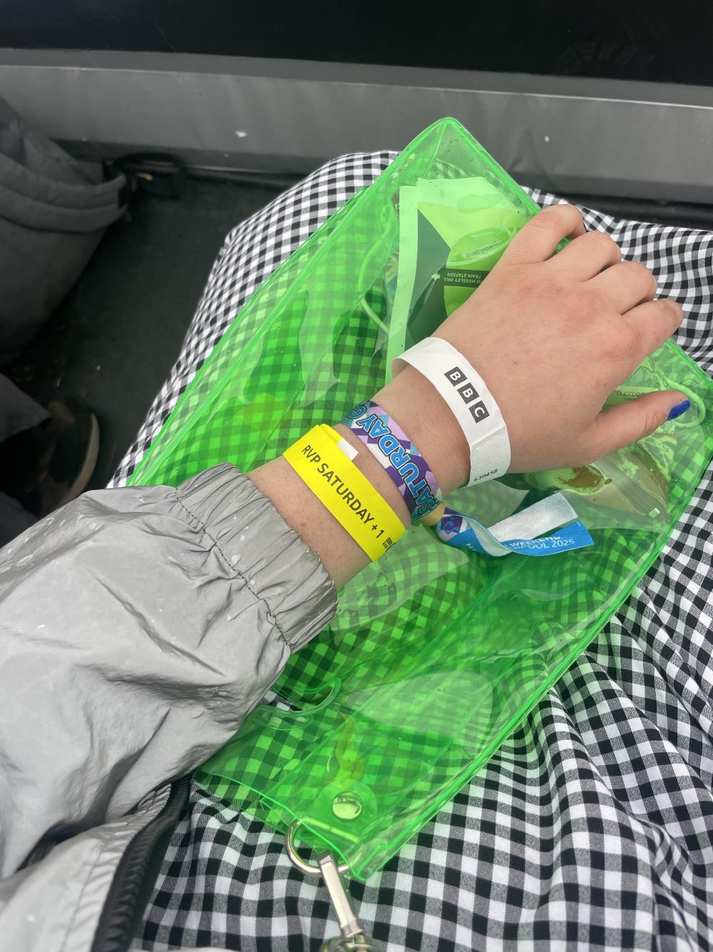 gab's arm with wristbands and the sleeve of a reflective jacket over a neon green translucent bag and a gingham skirt